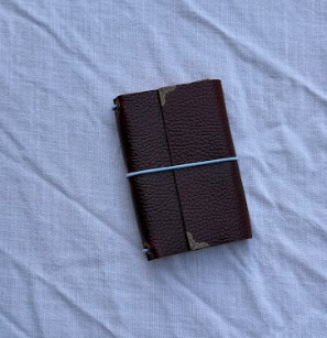 Red leather-bound journal with elastic band on a white fabric surface.