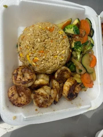 Fried rice with vegetables and grilled shrimp in a foam takeout container.
