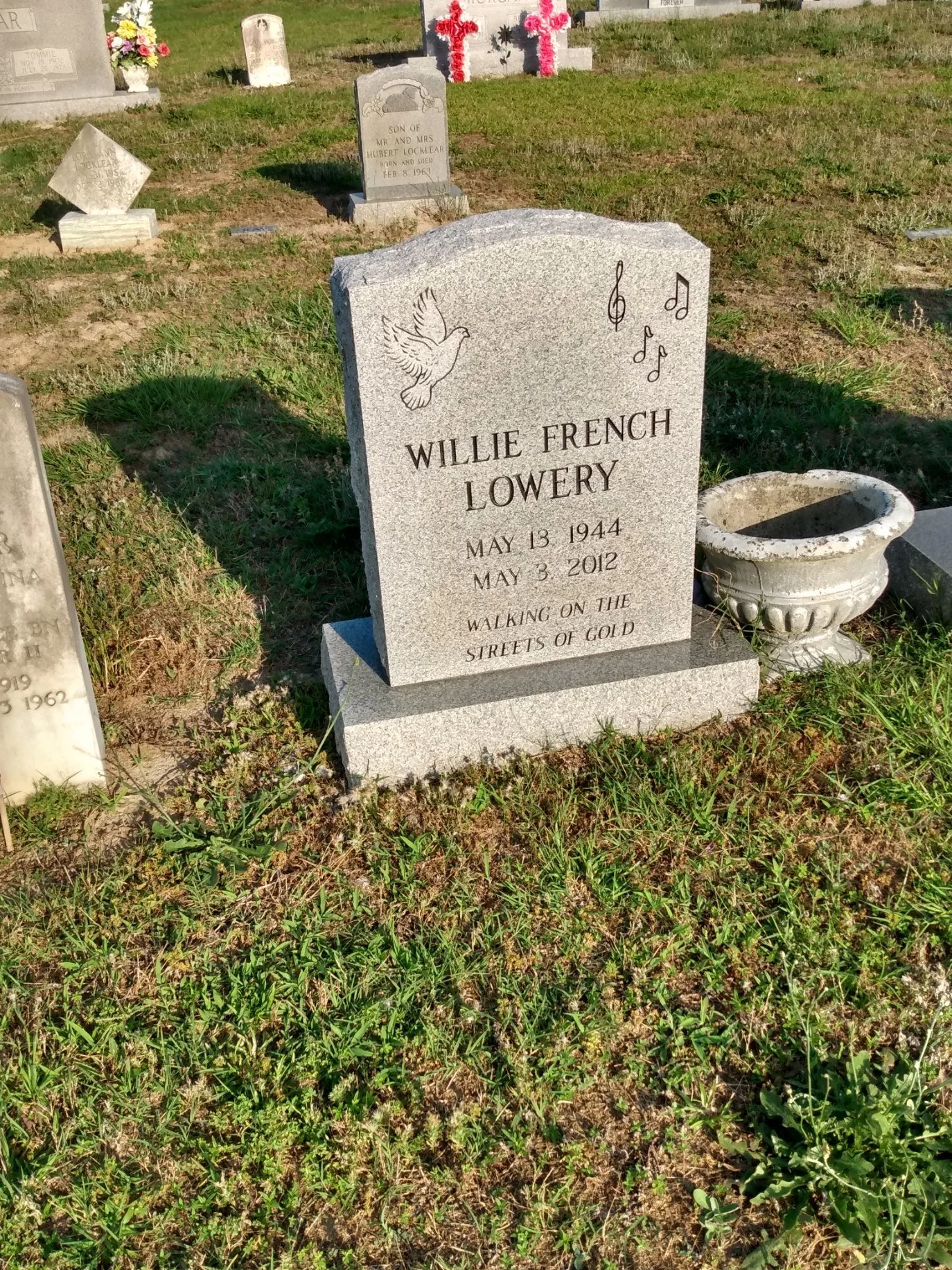 Gravestone with a dove illustration and musical notes in a cemetery, dedicated to Willie French Lowery, who was born on May 13, 1944, and died on May 3, 2012, with the inscription 'Walking on the streets of gold'.