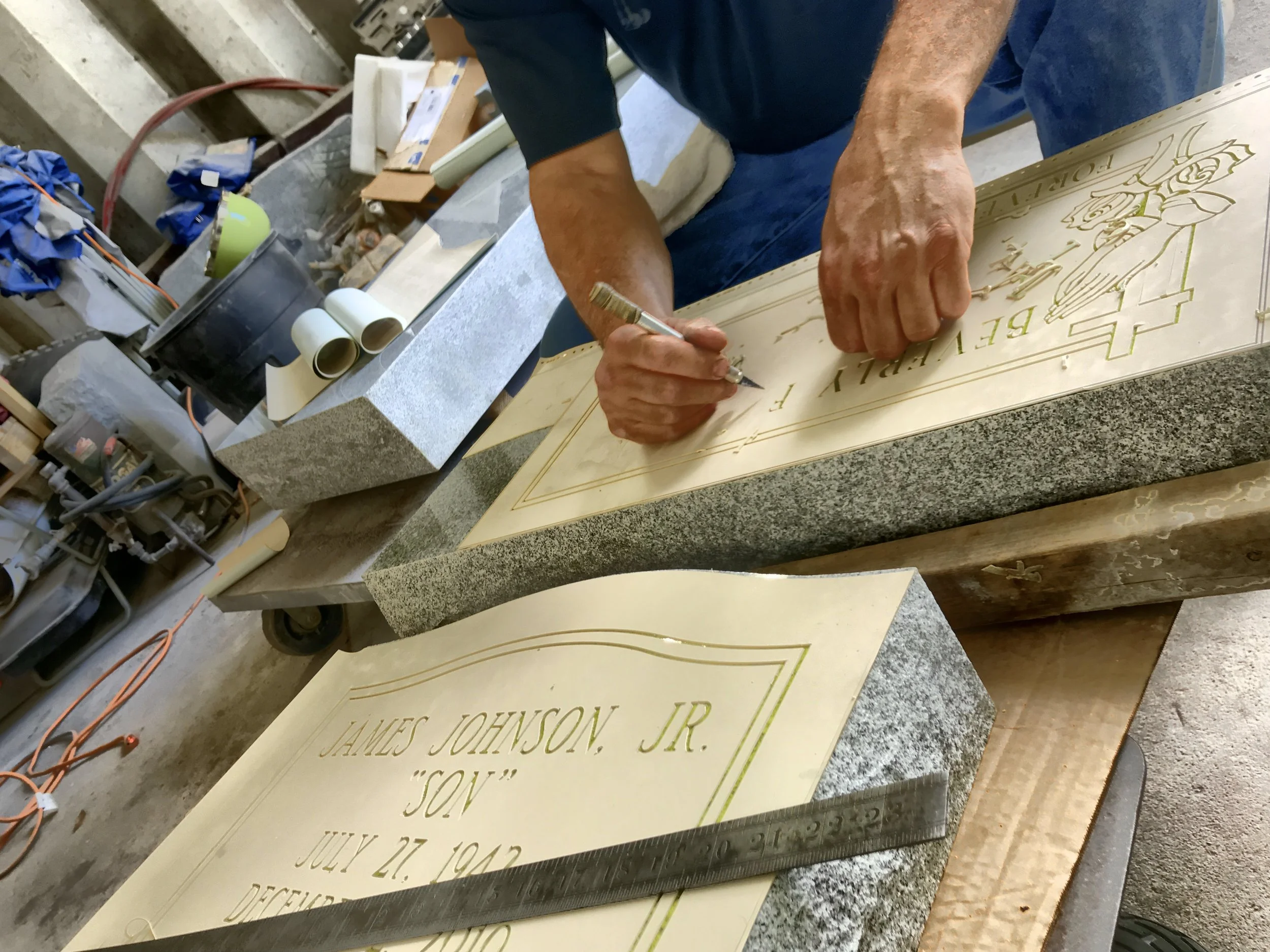 A person working on a grave marker for James Johnson Jr. in a workshop, with tools and materials nearby.