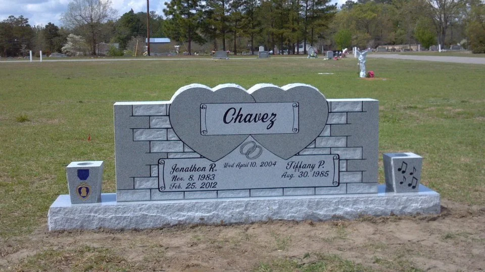 A gray granite headstone in a cemetery for the Chavez family. The headstone has a large heart at the top with two intertwined wedding rings. It displays the surname "Chavez" and the names of Jonathon R. and Tiffany P., along with their birth dates an
