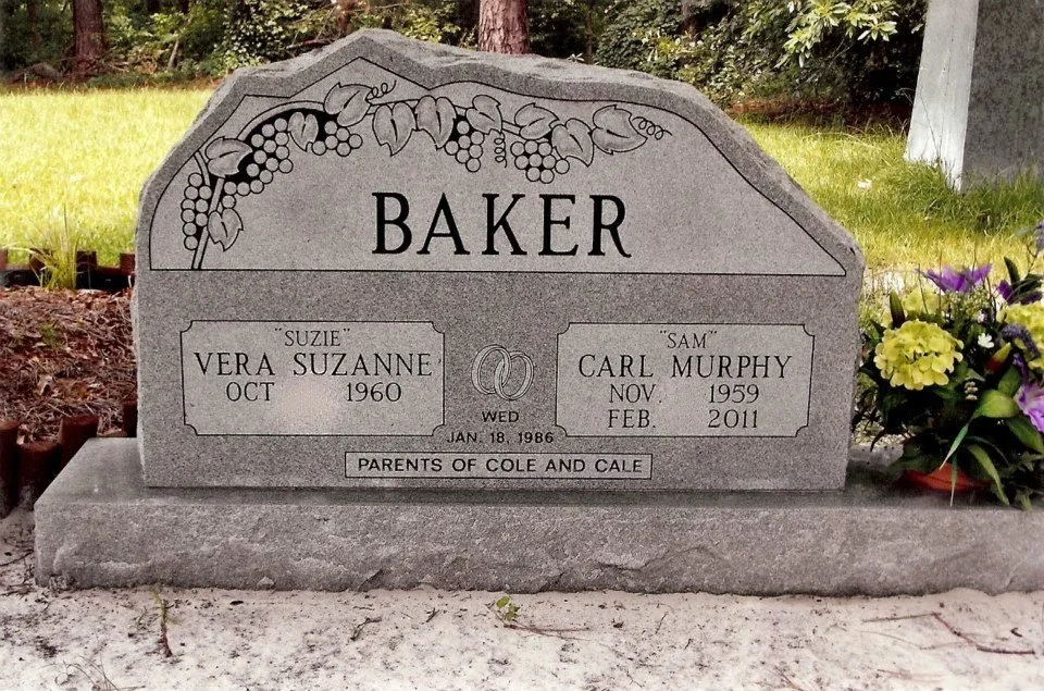 Gray granite tombstone for Vera Suzanne Baker and Carl Murphy Baker with decorative grapevine engraving at the top, floral arrangement on the right, and inscriptions including birth and death dates, marriage date, and family tribute.