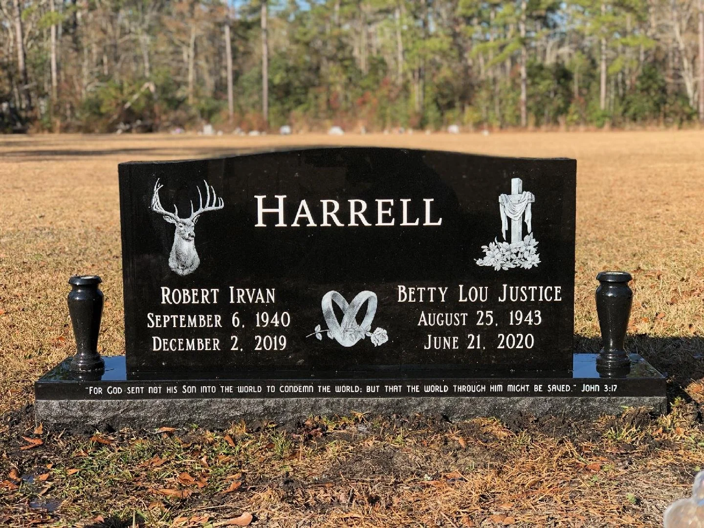Black granite headstone for Harrell family with deer head illustration on the left and Jesus crucifix with flowers on the right, inscriptions for Robert Irvan and Betty Lou Justice with birth and death dates, a clasp with a flower in the center, and 
