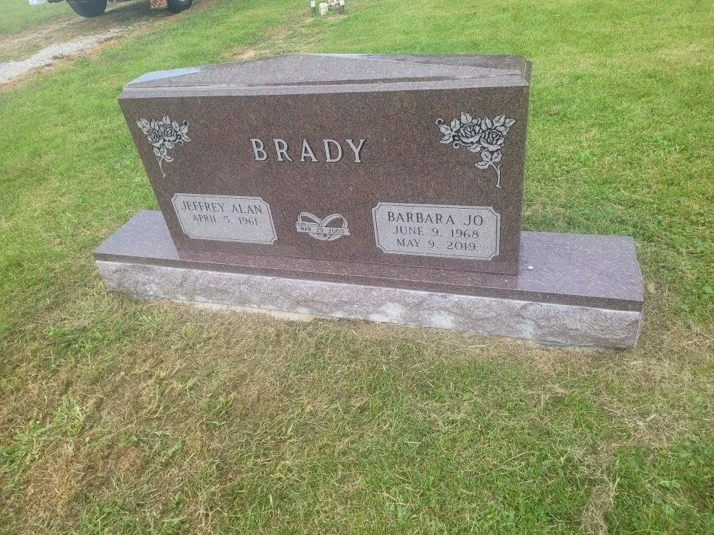 A polished granite headstone with the surname 'Brady' engraved at the top, decorated with floral carvings. It has two inscribed plaques: one for Jeffrey Alan, born April 5, 1961, died April 29, 2000, and another for Barbara Jo, born June 9, 1968, and