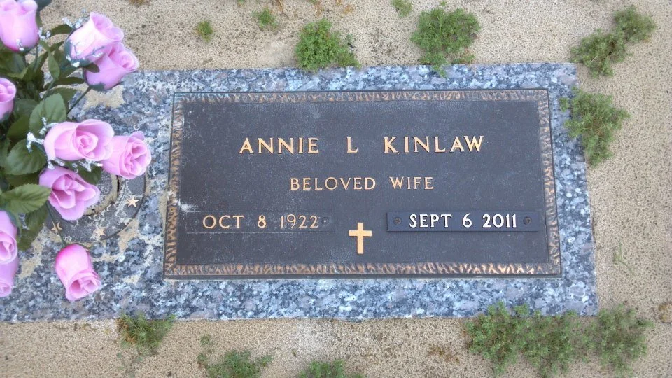 Gravestone for Annie L. Kinlaw, born October 8, 1922, and died September 6, 2011, with a bouquet of light purple roses placed beside it.