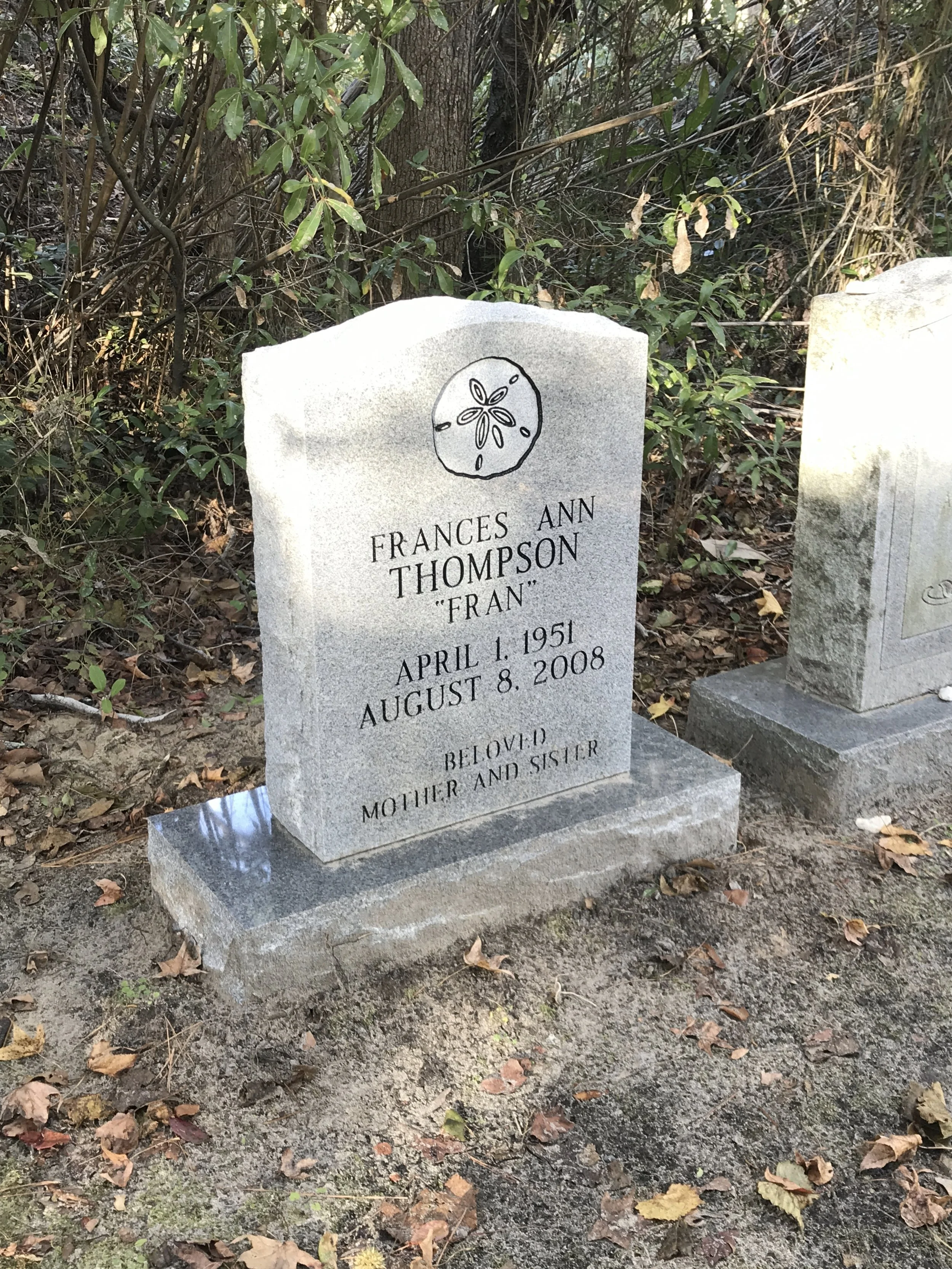 Gravestone in a cemetery with a carved flower design at the top, inscribed with the name Frances Ann Thompson, nicknamed Fran. Dates of birth April 1, 1951, and death August 8, 2008, are visible. The gravestone is surrounded by fallen leaves and othe