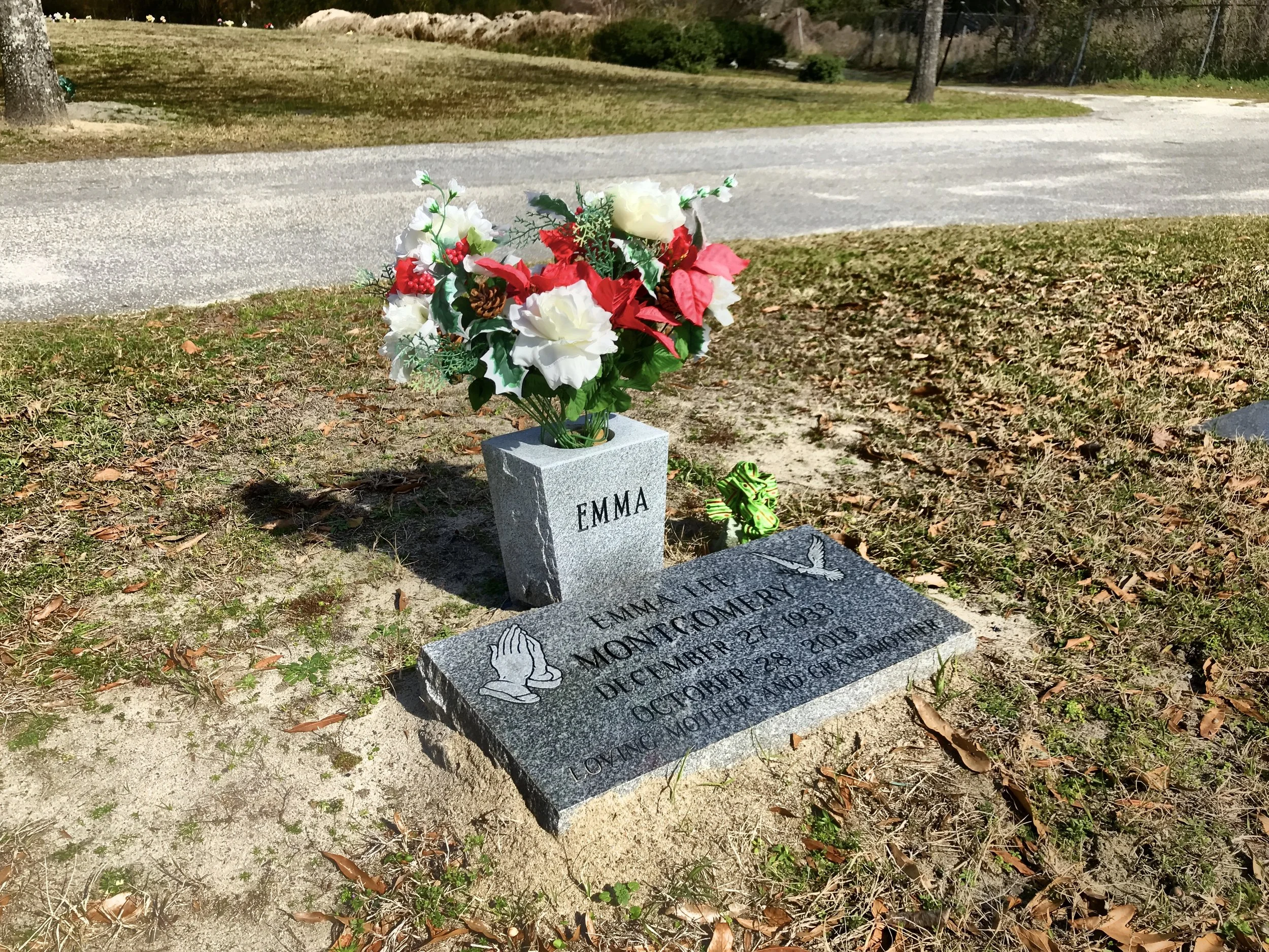 Personalized gravestone with flowers and a small green ribbon in a cemetery.