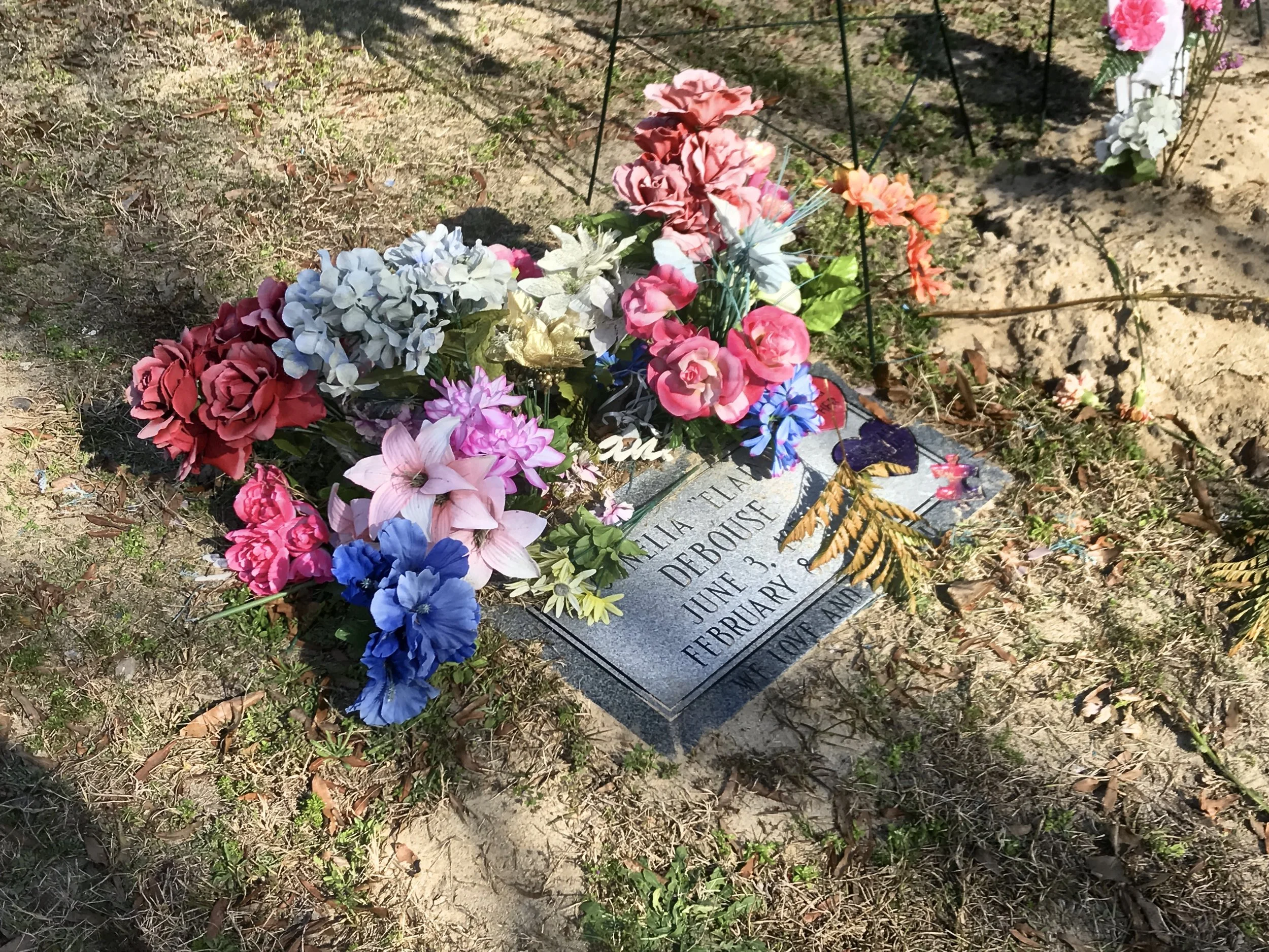 A grave marker surrounded by colorful artificial flowers on the ground.