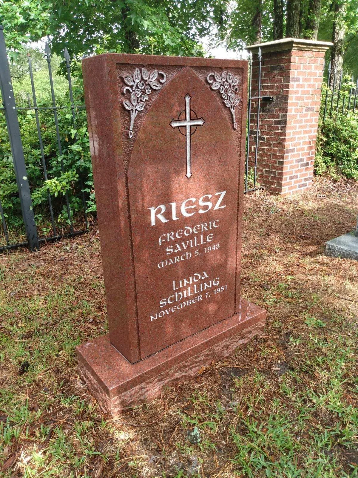 Gravestone for Frederic Saville Riesz and Linda Schilling, located outdoors with green trees and a brick fence in the background.