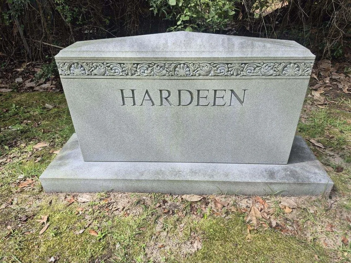 Gray granite headstone with the name 'HARDEN' engraved on it, situated on grass with some leaves nearby.