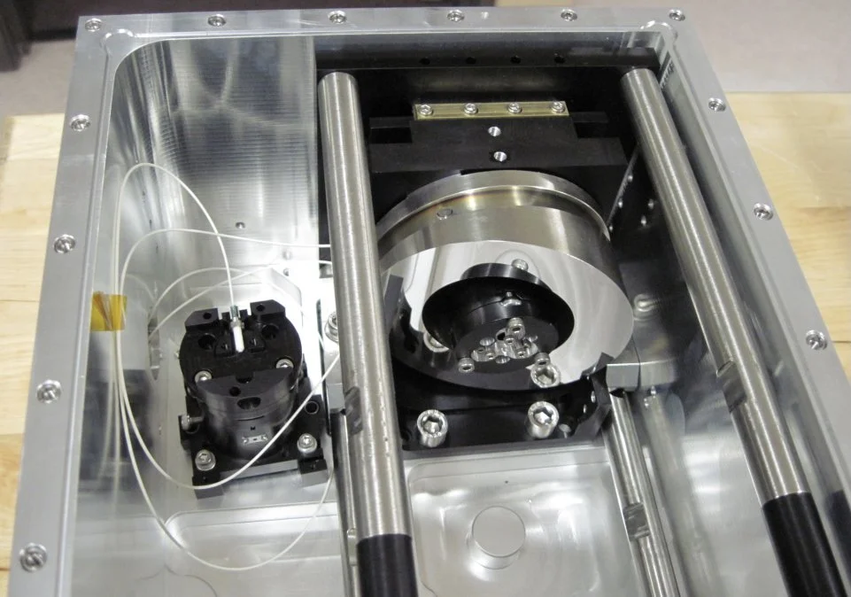 Close-up of a scientific or industrial machine with metallic components, cylindrical rods, and wiring inside a metal frame.