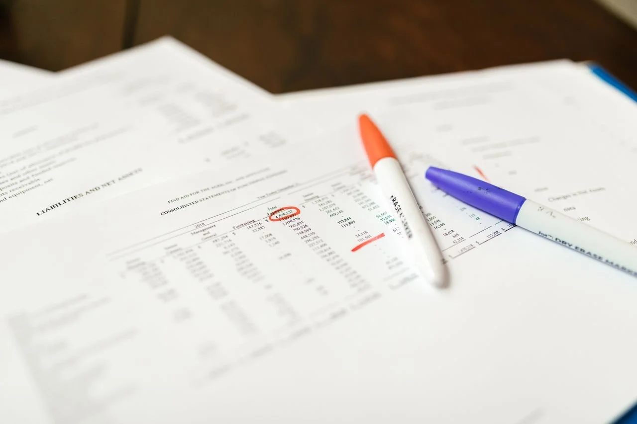 Financial documents with two markers, one orange and one blue, on a wooden table. | Northstar Trust Accounting | HOA Financials | Monthly Reconciliation | AppFolio | DRE Compliance