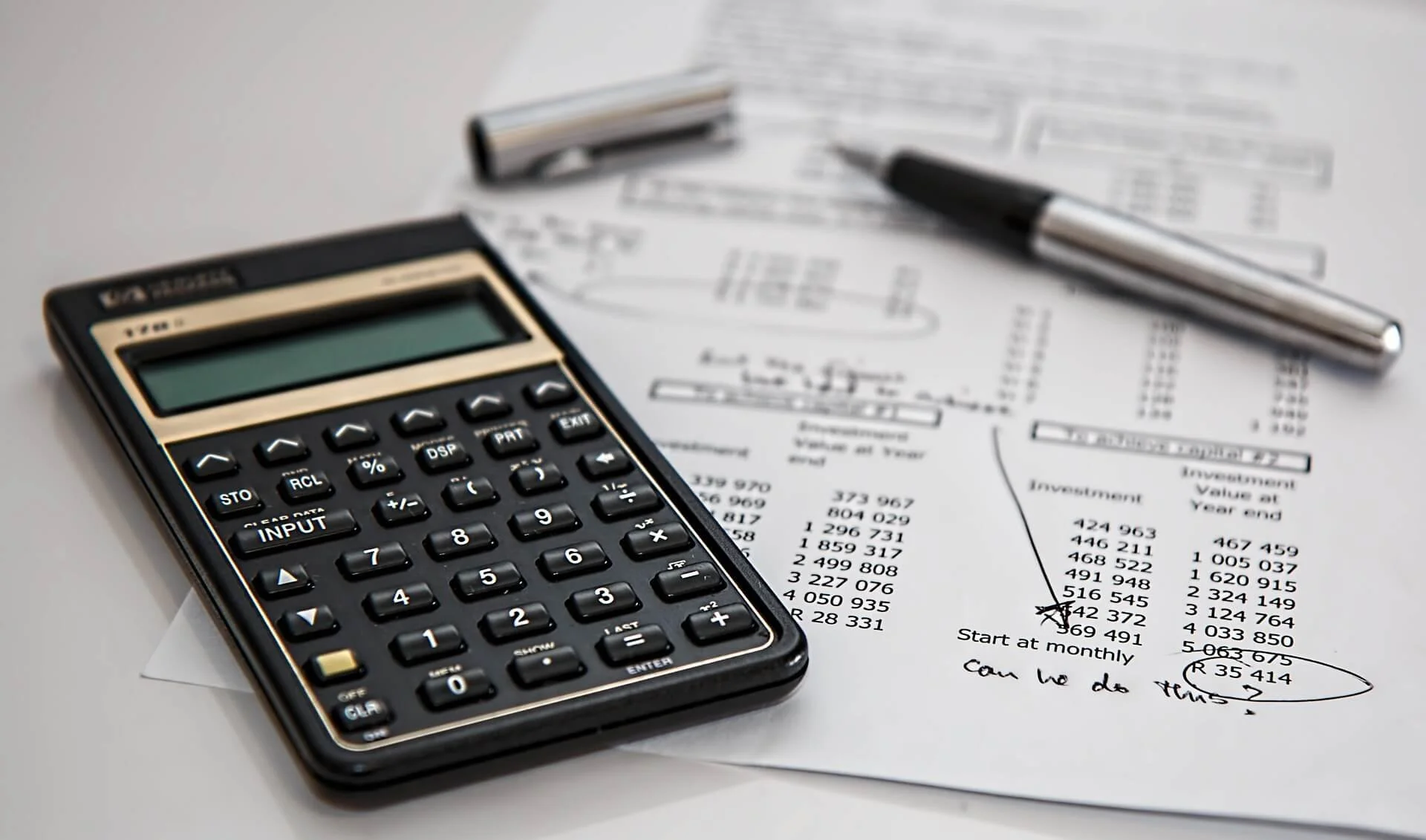 A calculator, a black pen, and printed financial documents on a white surface. | Northstar Trust Accounting | HOA Financials | Monthly Reconciliation | AppFolio | DRE Compliance