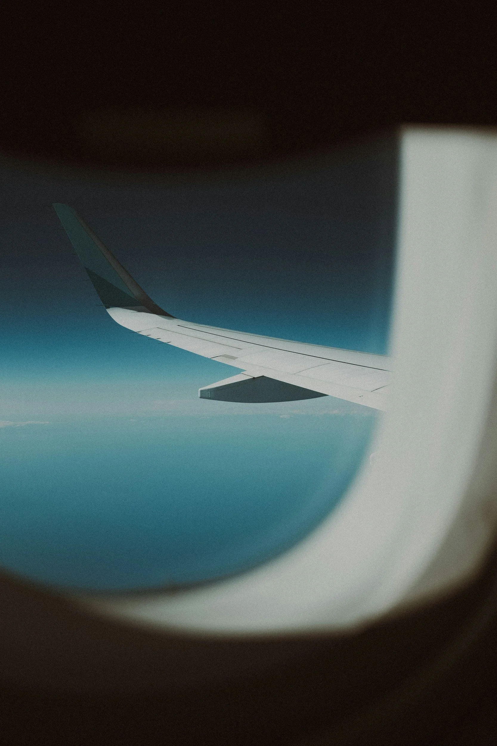 View from an airplane window showing the wing with a dark sky and clouds underneath.