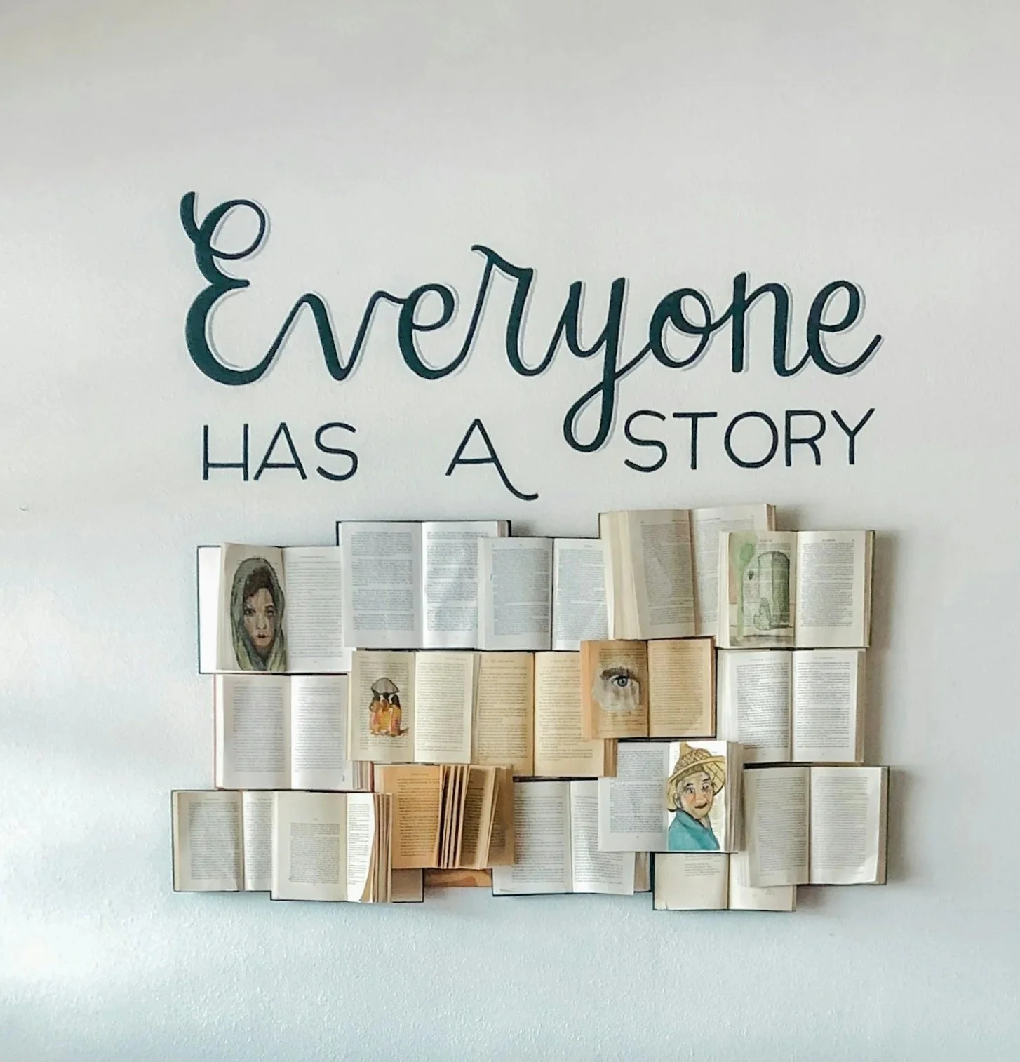 Wall display with the quote 'Everyone has a story' above pages of books and illustrations, including portraits and drawings.
