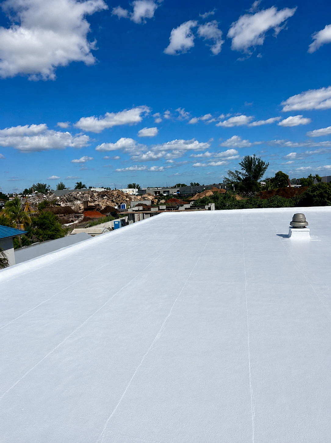 A flat white rooftop with a vent in the right corner, under a partly cloudy blue sky.