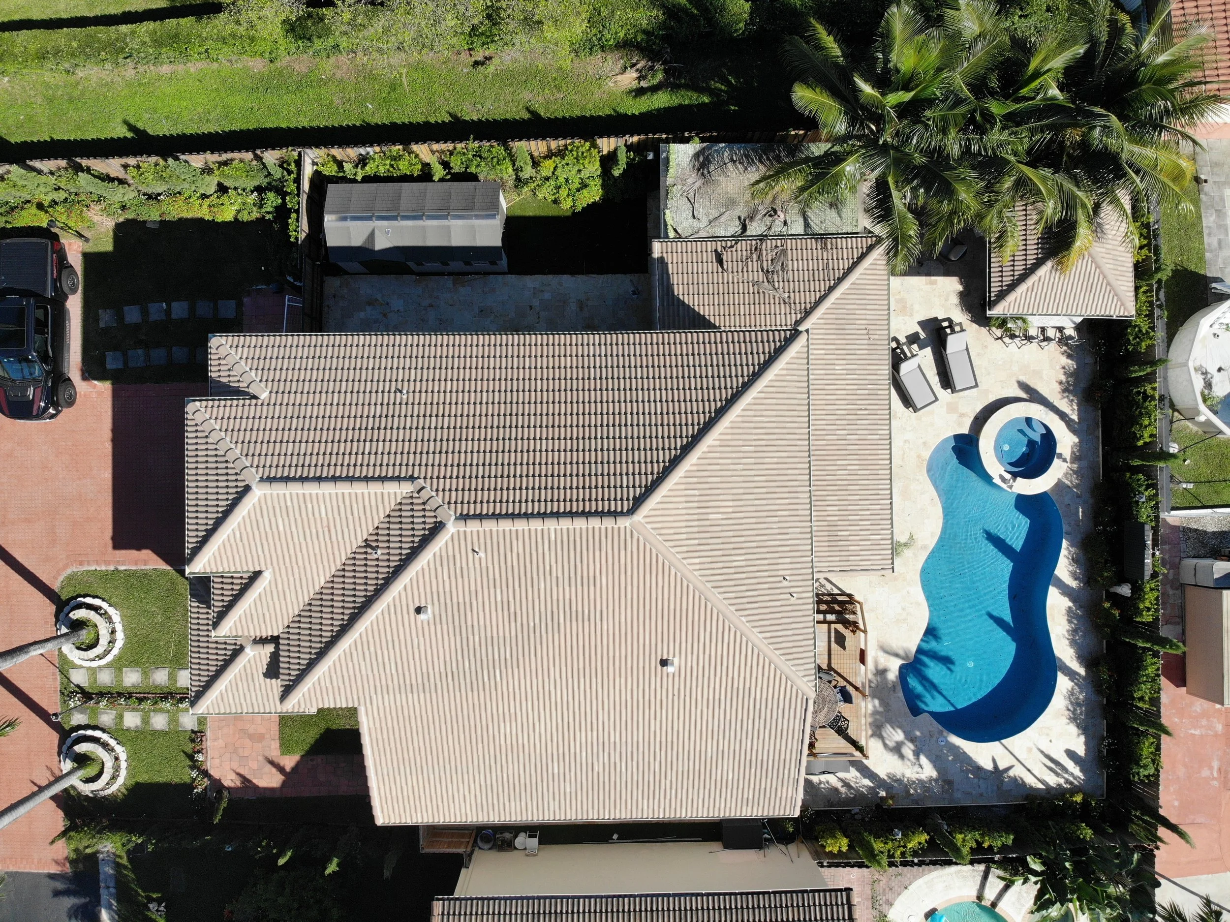 An aerial view of a backyard with a swimming pool, patio furniture, a shaded area, a small garden, and tall palm trees.