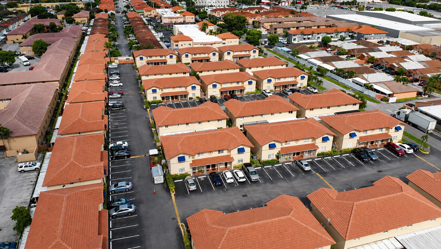 An aerial view of a residential neighborhood showing multiple houses with tiled roofs, palm trees, and front yards.