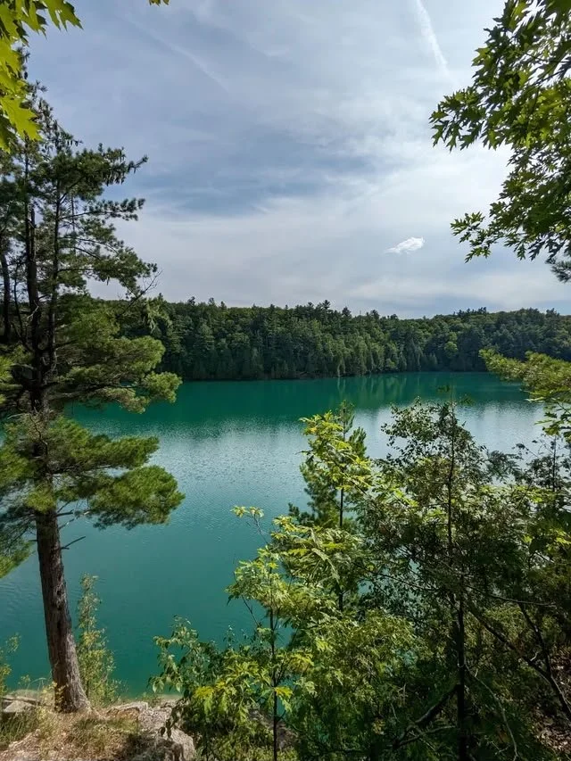 A scenic lake surrounded by lush green trees with a partly cloudy sky overhead.