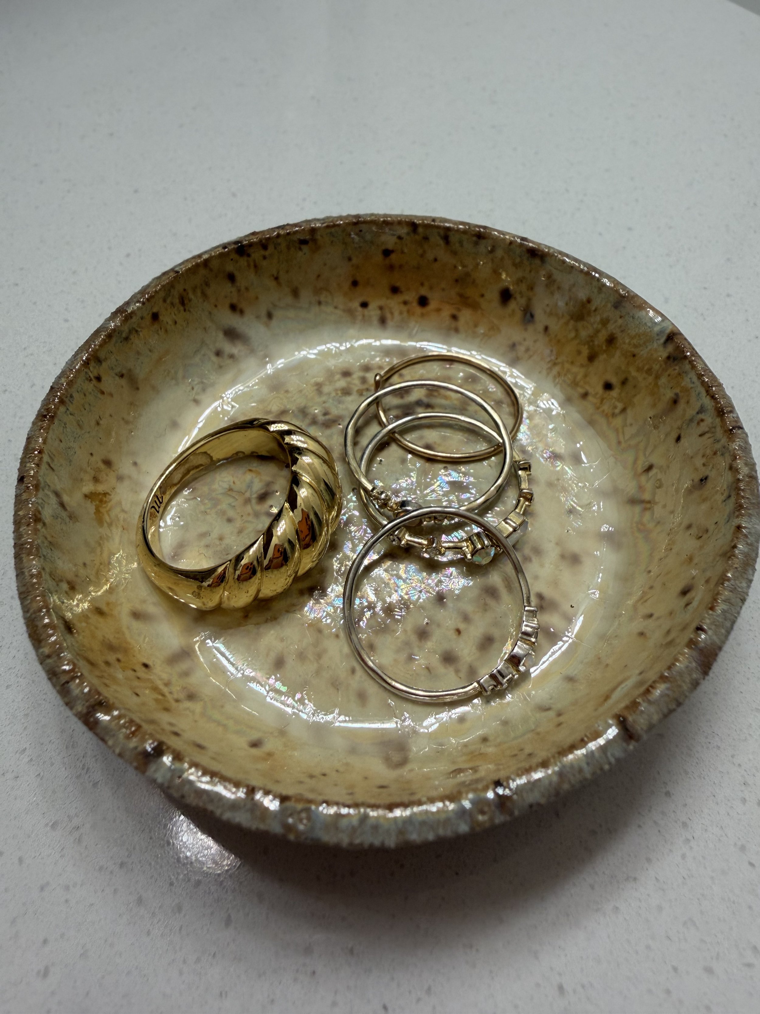 Ceramic bowl with jewelry, including rings and earrings, on a white surface.