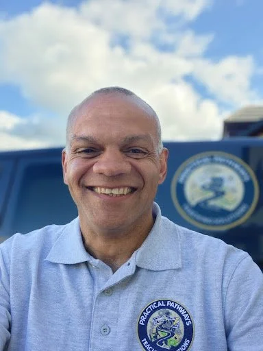Smiling portrait of Des Stokes, founder of Practical Pathways, wearing a grey polo shirt with the company logo.