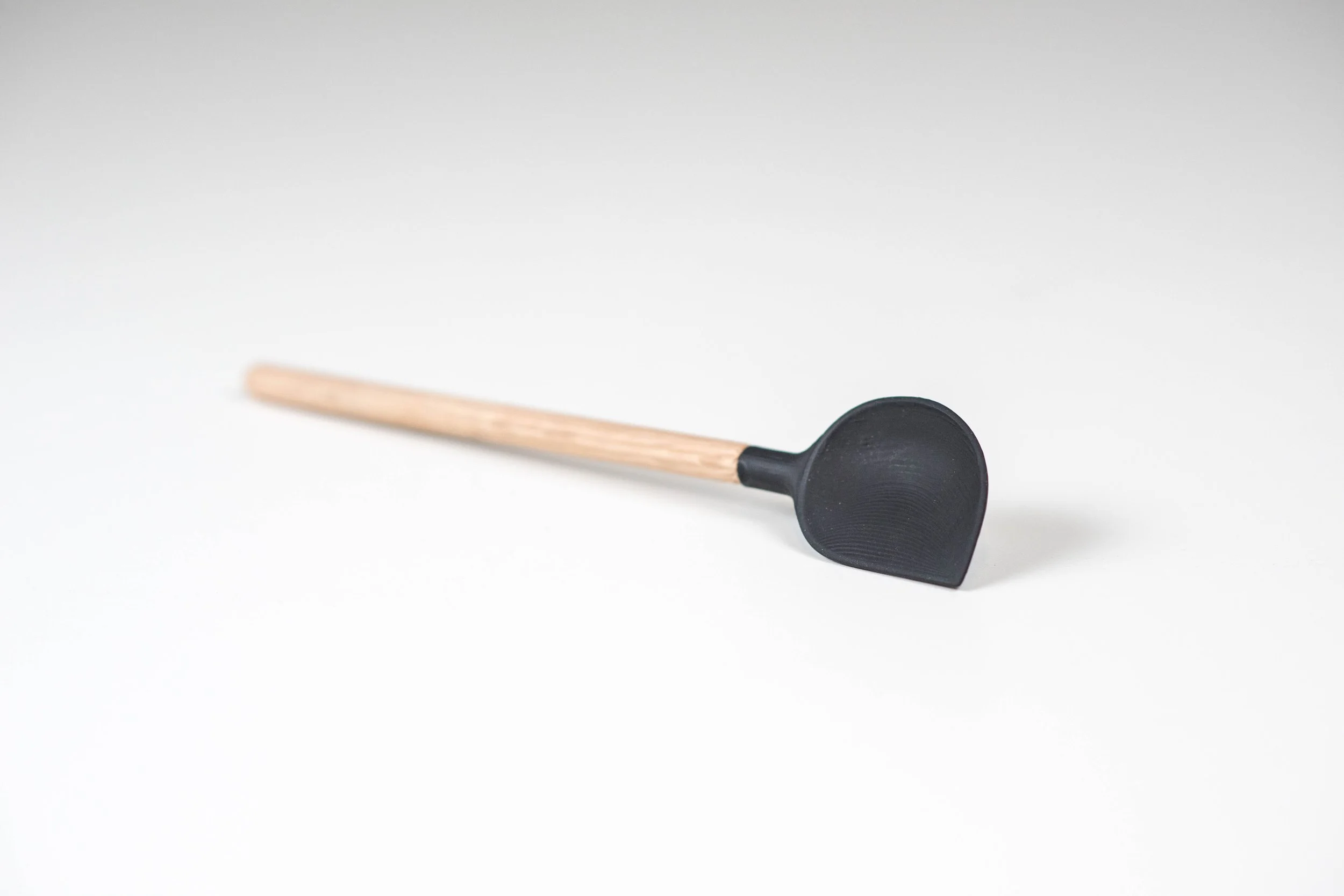 A black spoon sample with a wooden handle resting on a white surface.