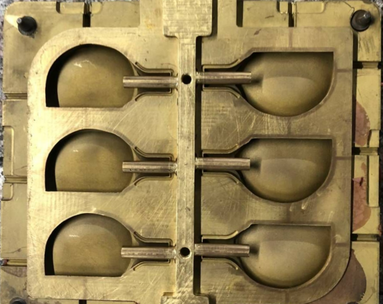 Close-up of a metal mold with three cavities in the shape of spoons, used in manufacturing or cooking.