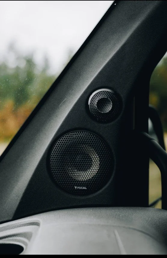 Close-up of a black car interior showing a Focal speaker with two smaller speakers above it, mounted on the A-pillar.