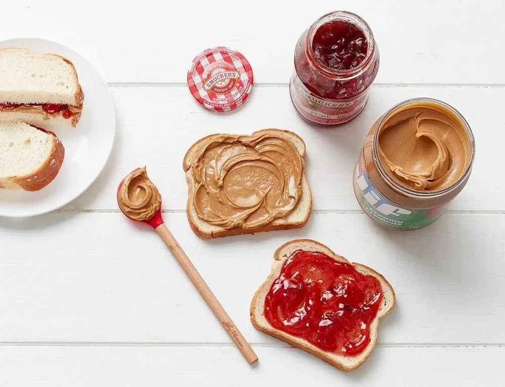 Peanut butter and jelly sandwiches with a jar of grape jelly and peanut butter on a white surface.