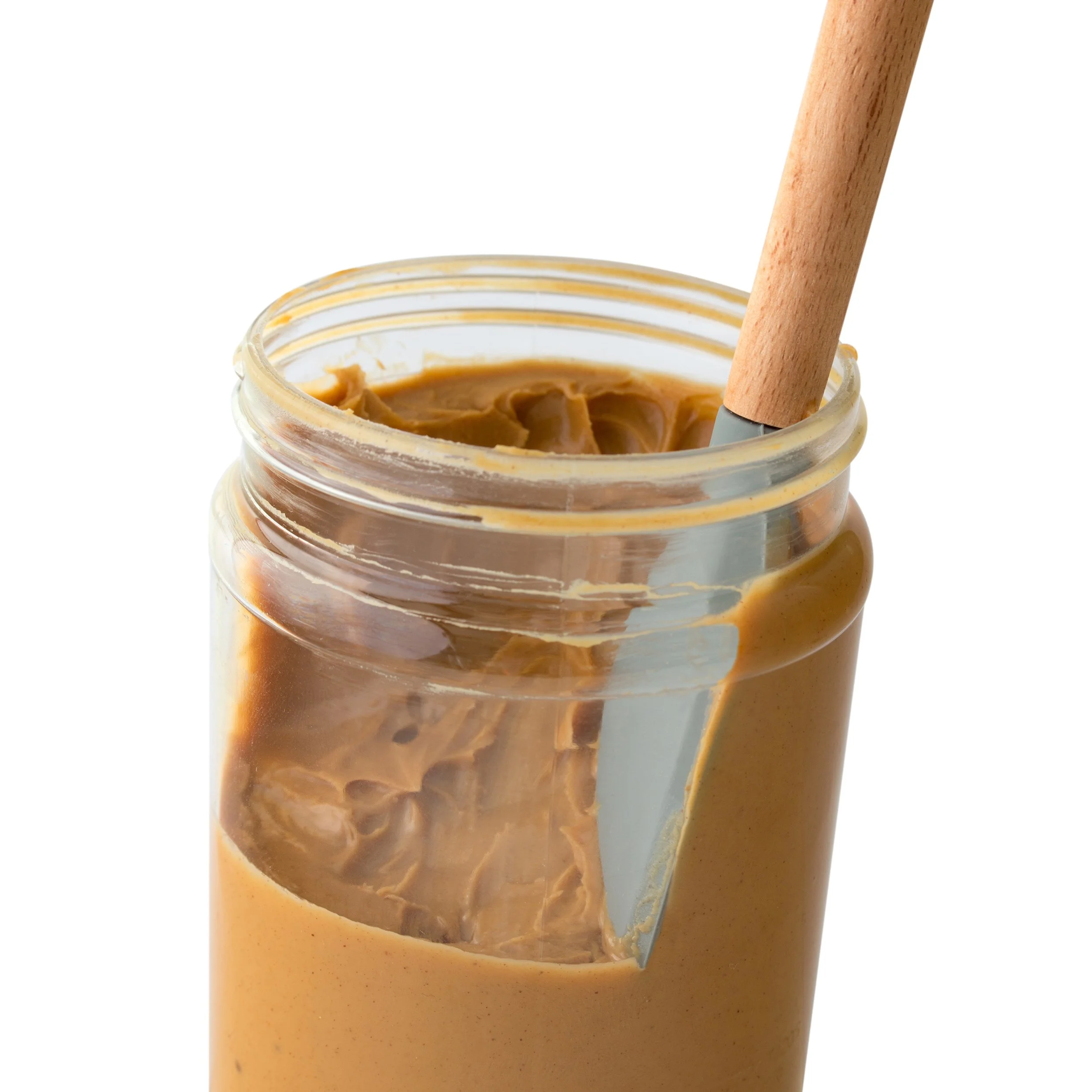 Close-up of a glass jar filled with peanut butter with a wooden spoon inside.