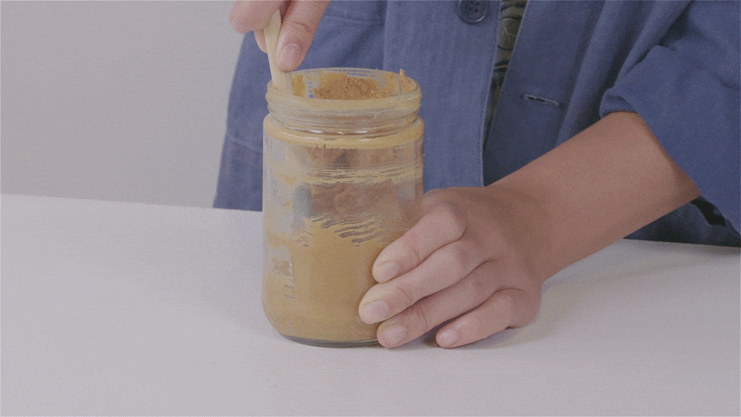 Person scooping peanut butter from a jar with a spoon.