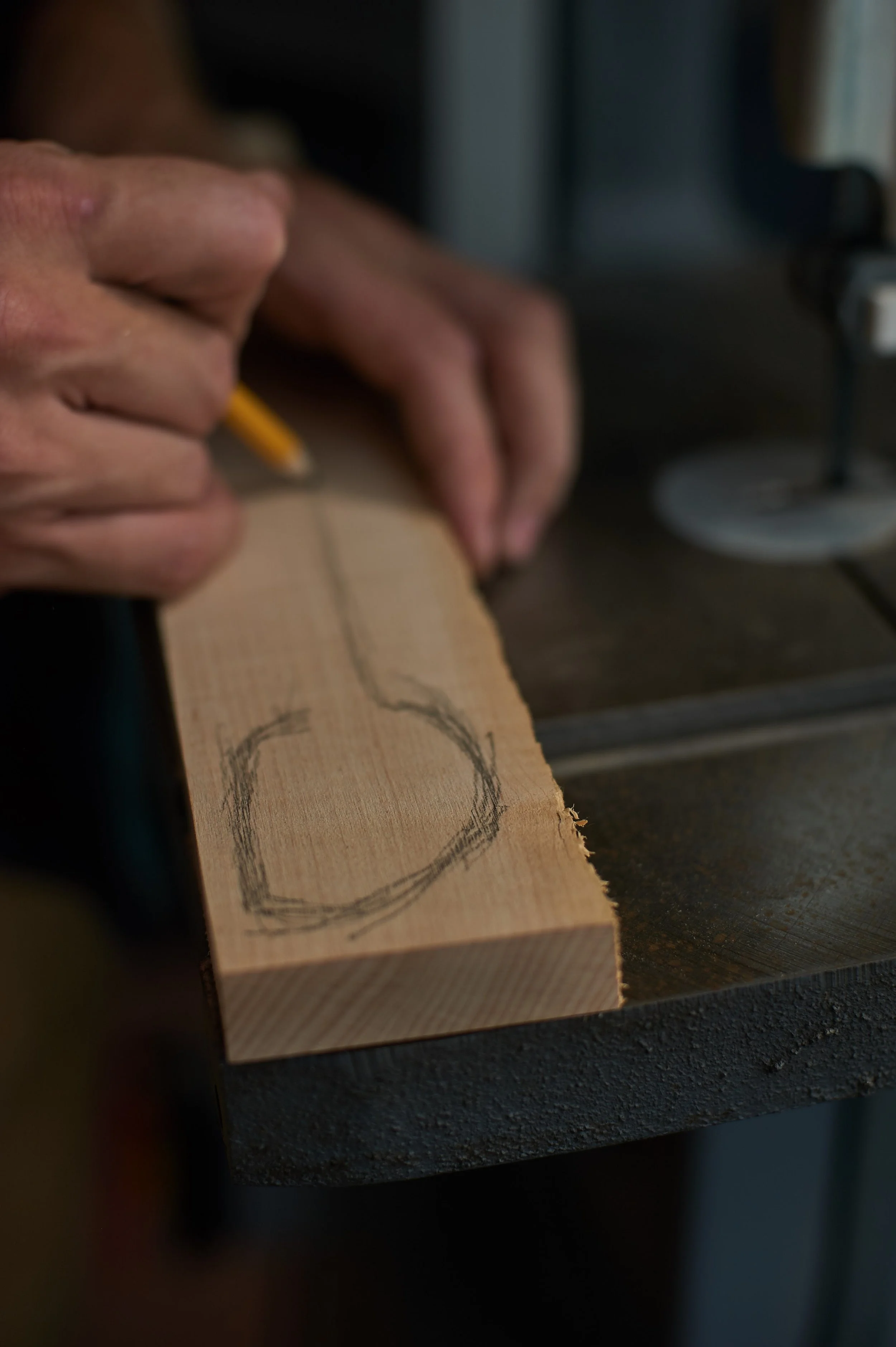 Close-up of a hand holding a yellow pencil, drawing a circle on a piece of wood with a hand-drawn circle outline.