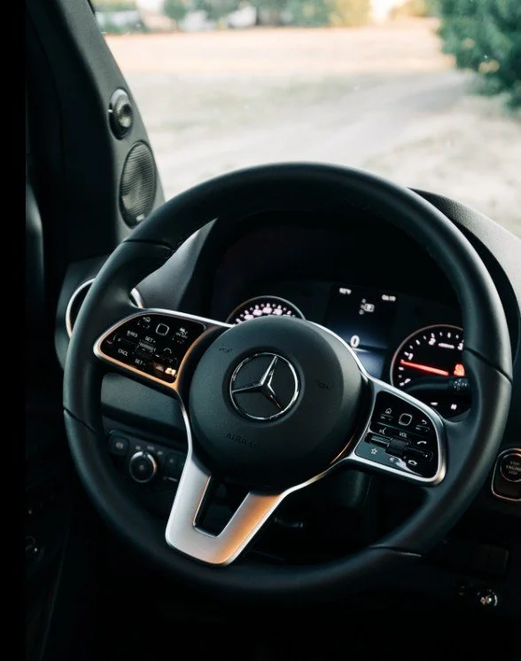 Close-up of a Mercedes-Benz steering wheel with digital dashboard visible in the background, parked outdoors.