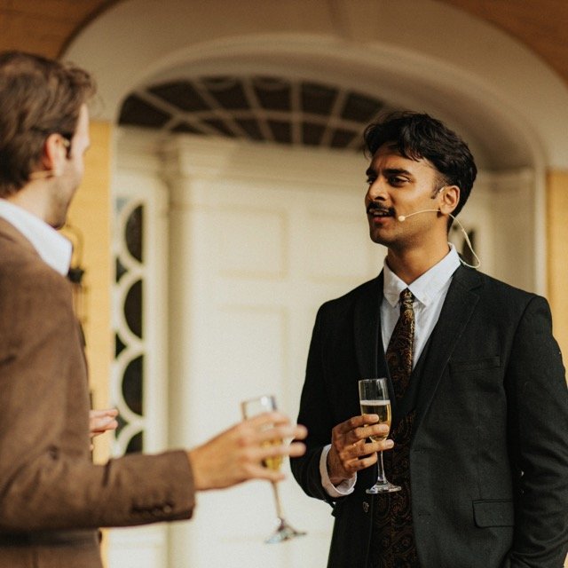 Two men in formal attire having a conversation at a social event, holding glasses of champagne.