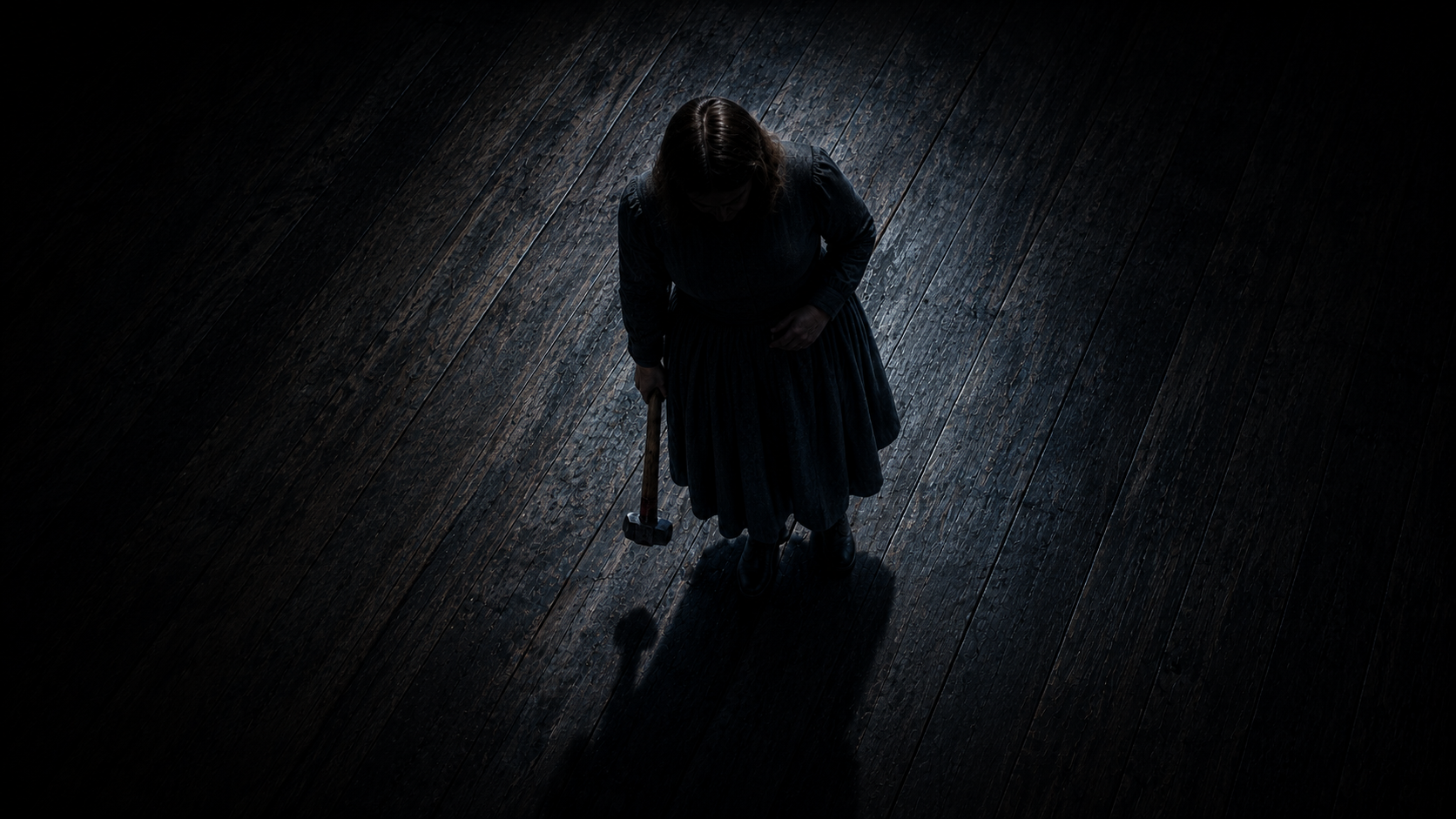 A woman dressed in dark clothing standing on a wooden floor holding a hammer, with a shadow cast in low light.