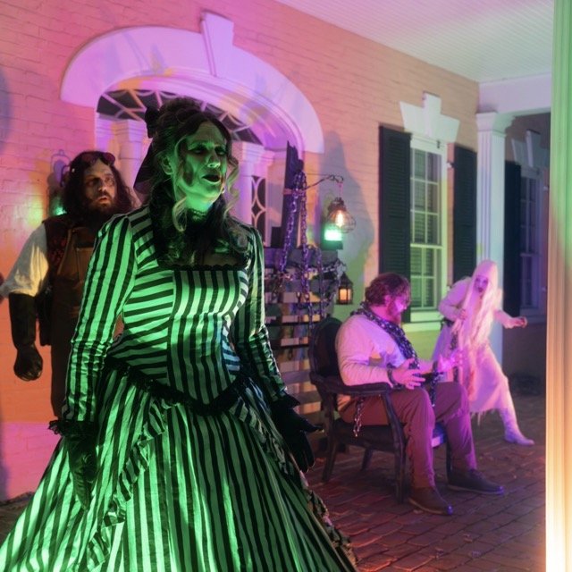 People dressed in costumes performing a theatrical show on a porch with colorful lighting.