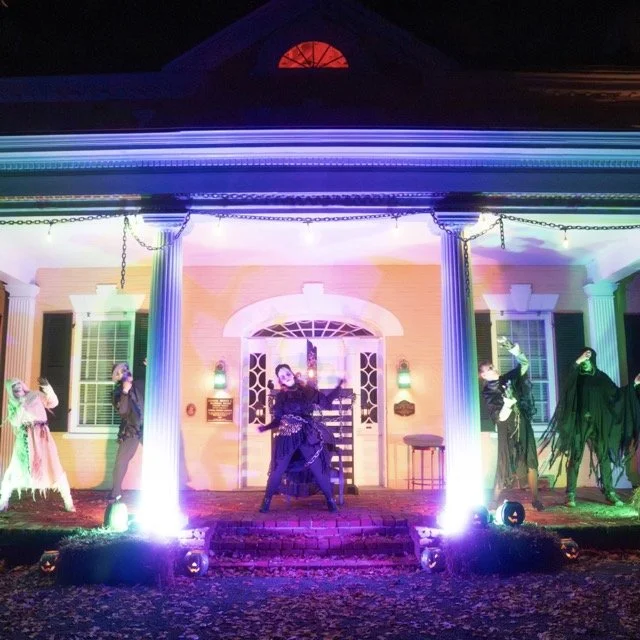 House decorated with colorful lights and Halloween-themed costumes on porch