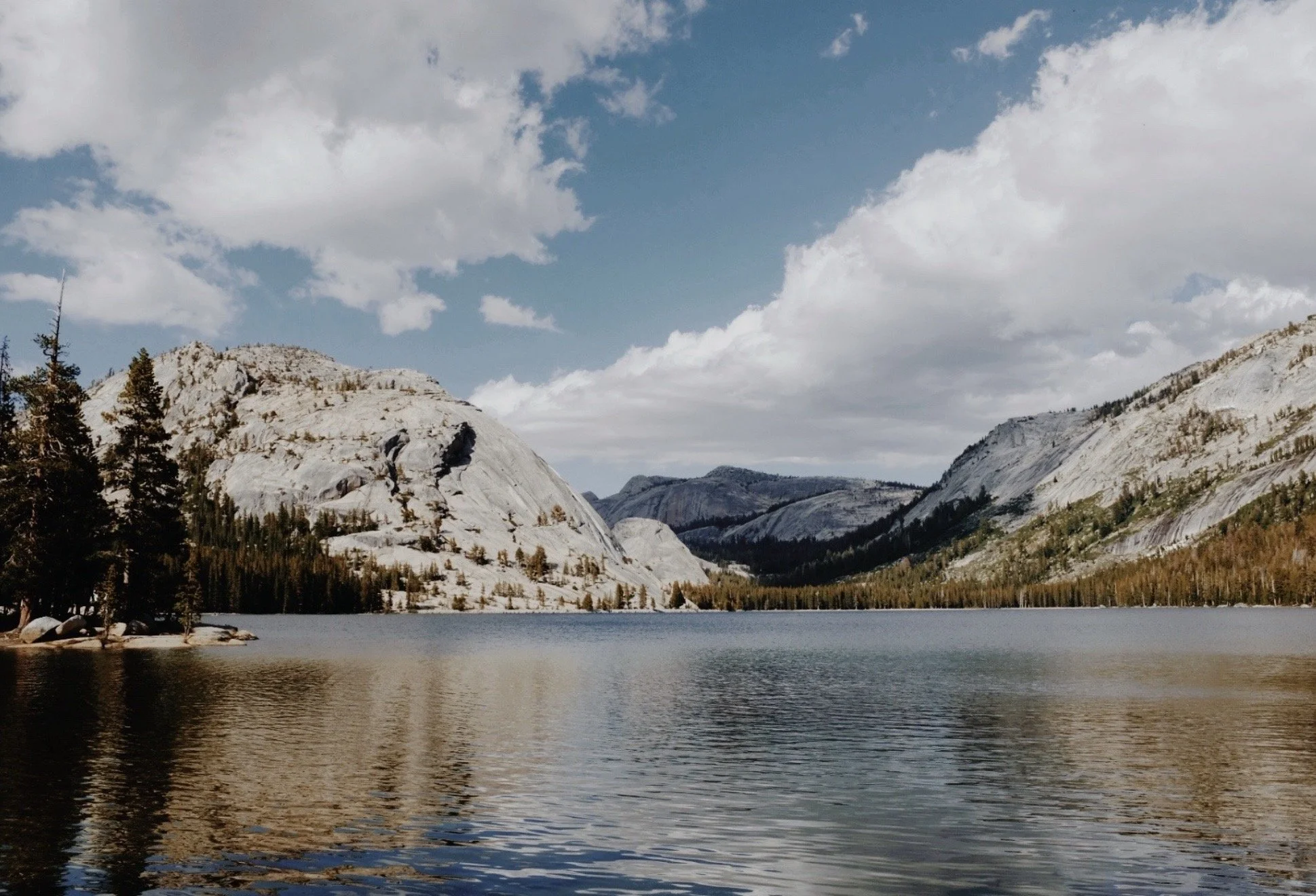 A scenic view of a lake surrounded by rocky mountains and pine trees under a partly cloudy sky.
