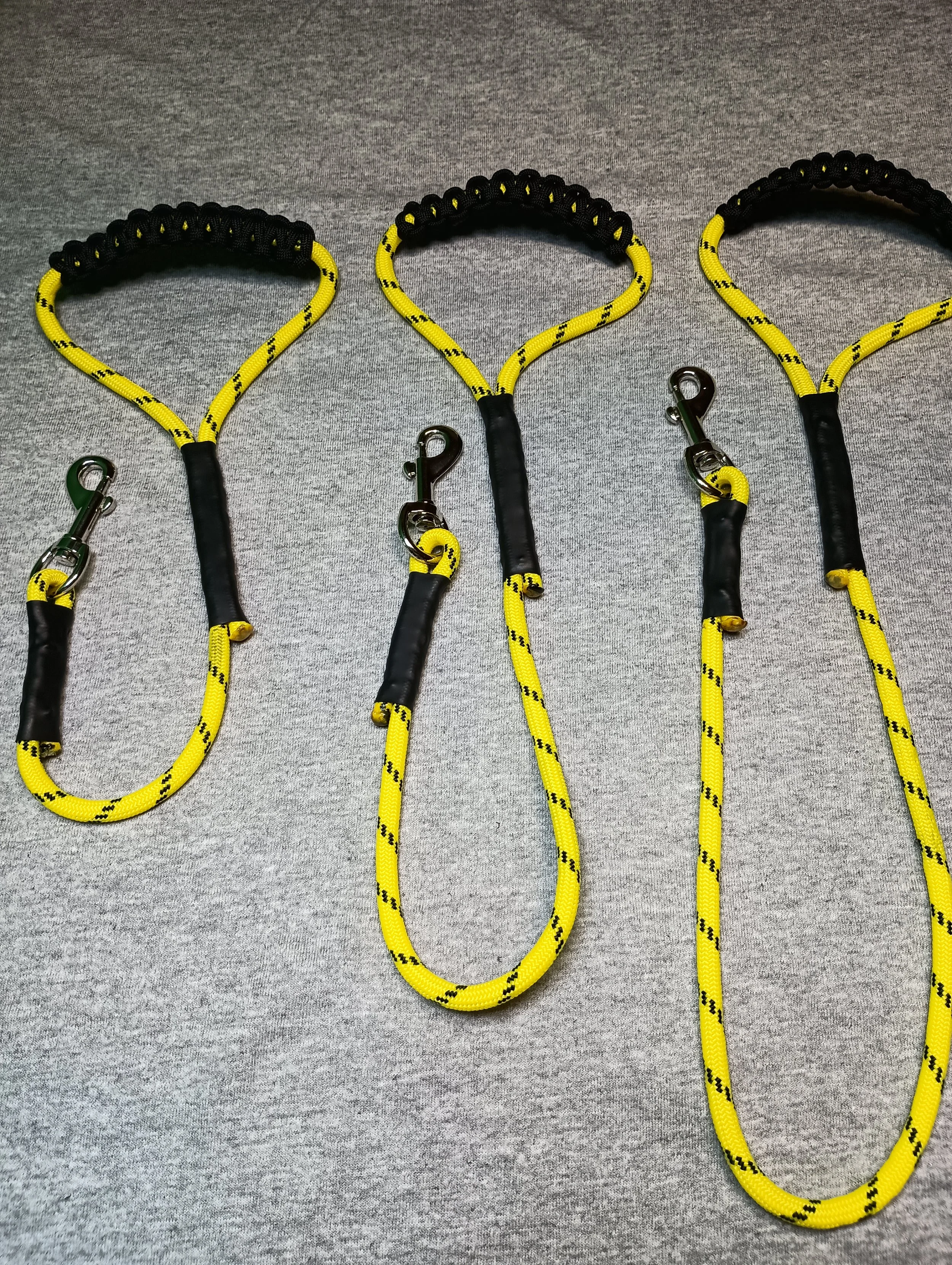 Three yellow bungee cords with black hooks and black padded grips laid on a gray surface.