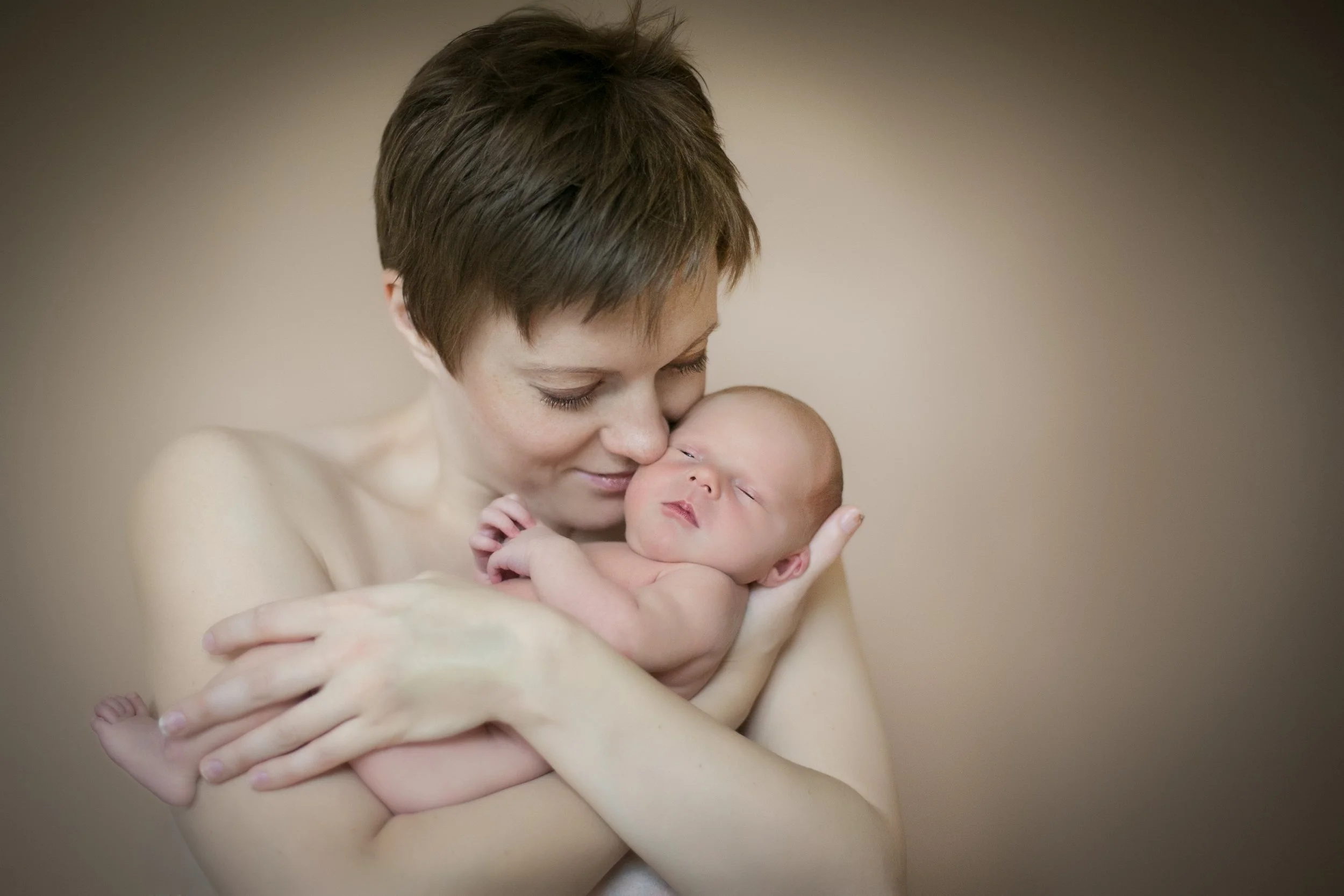 A mother holding her newborn baby skin-to-skin during an at-home mother and baby photography session in Bromley, London.