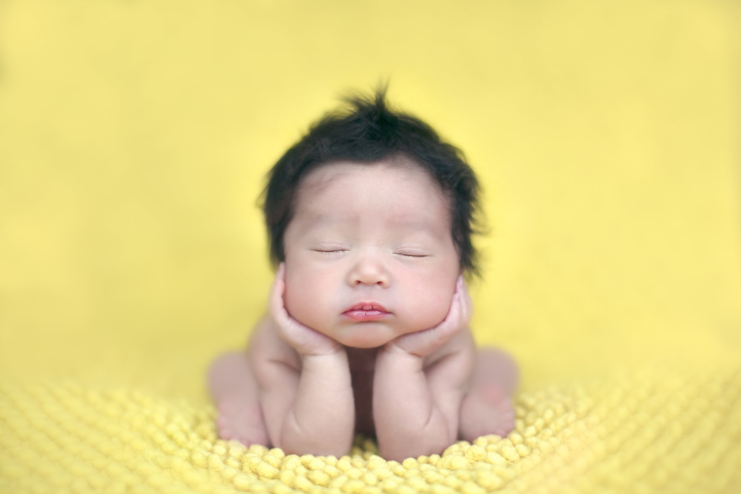 Classic posed newborn portrait — baby resting with hands under chin on a soft yellow blanket, photographed at home in South East London by Kate See.