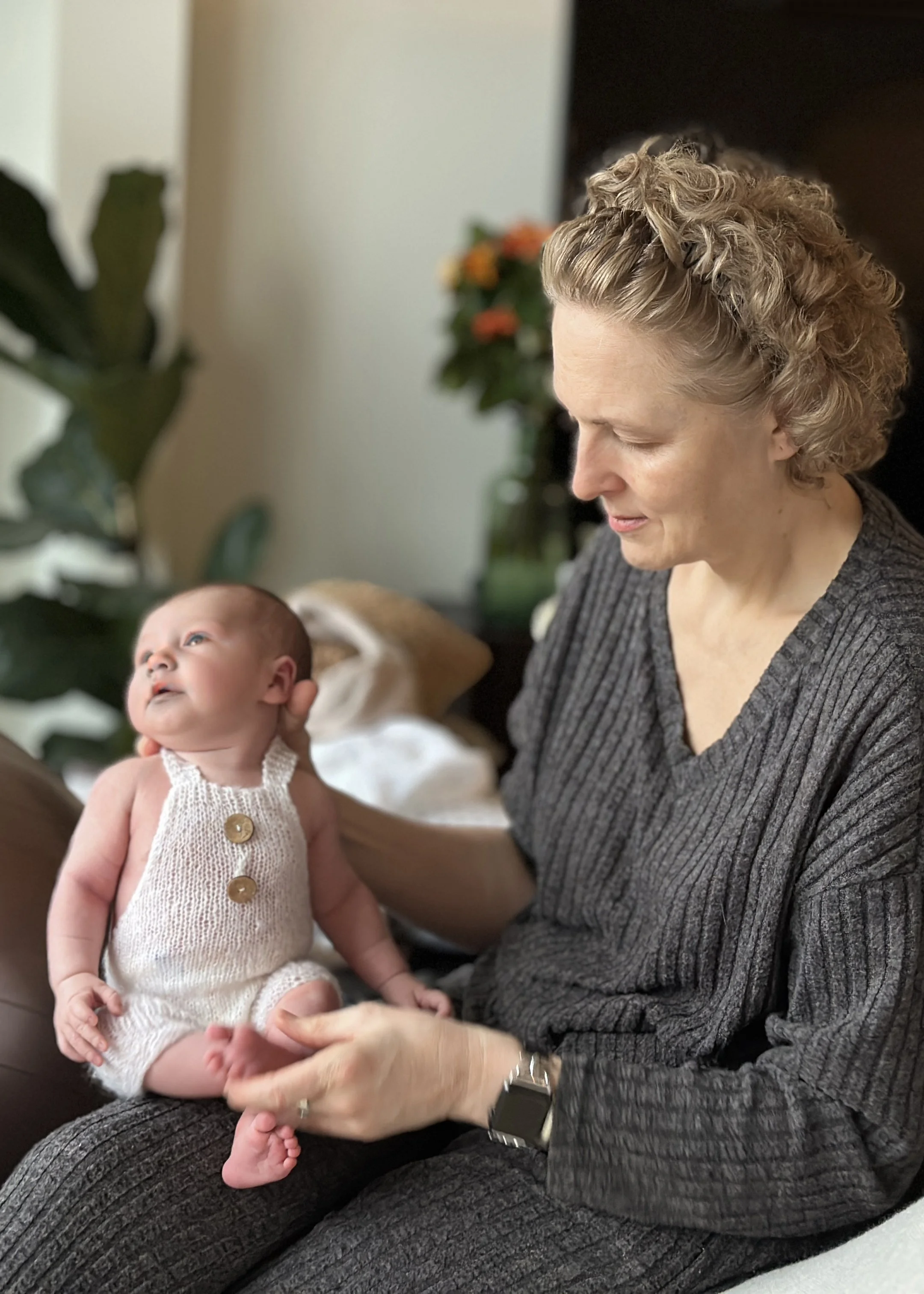 Newborn photographer Kate See holding a sleeping baby in a beige knit wrap during an at-home posed newborn session in Bromley, London.