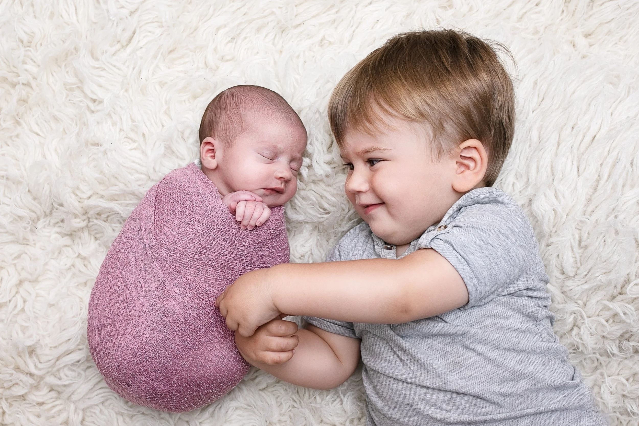Big brother gently meeting his newborn sibling during an at-home sibling newborn photography session in London by Kate See.