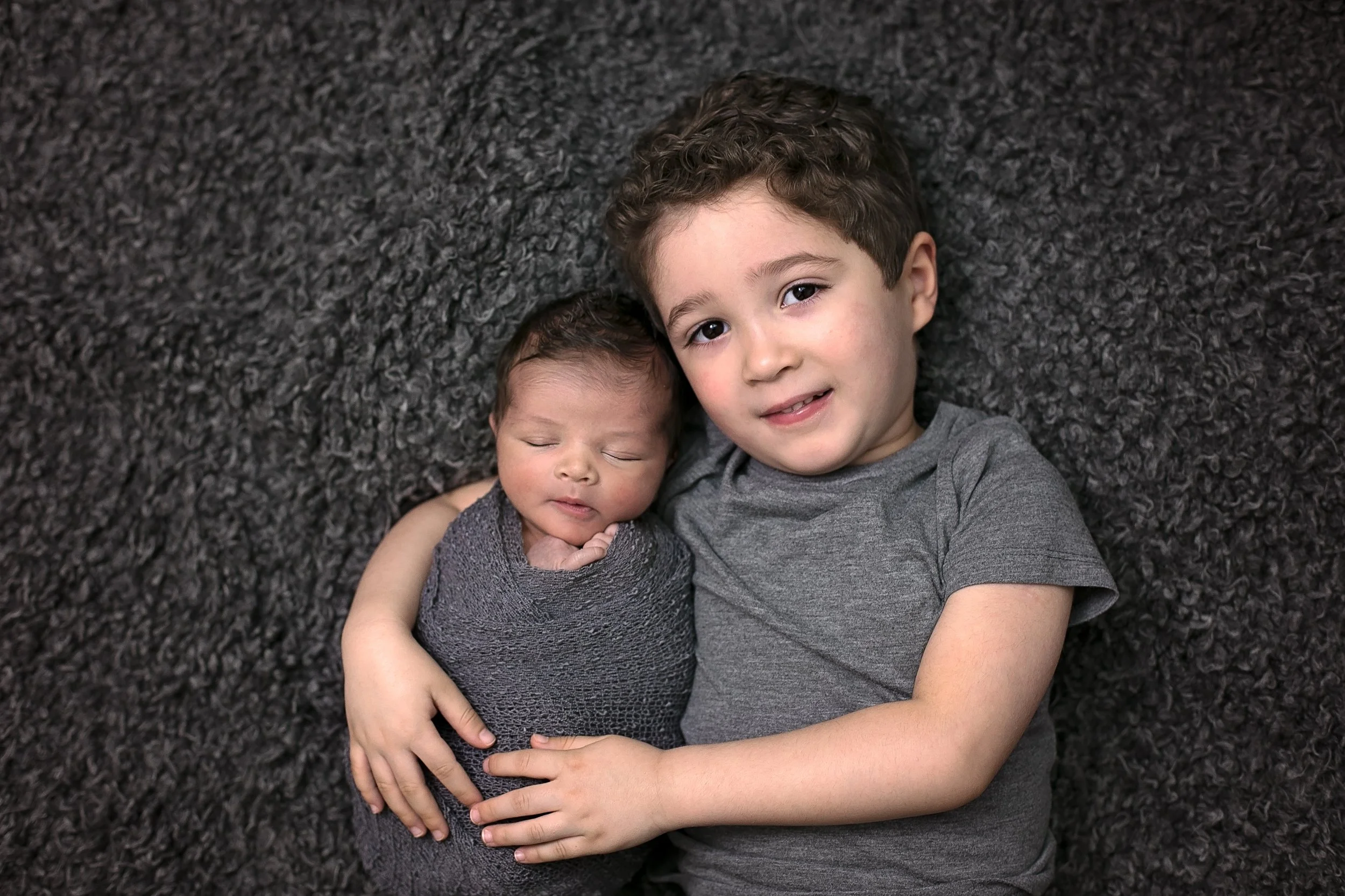 Toddler brother is with his newborn baby sibling during an at-home sibling newborn session in Bromley, London by Kate See.
