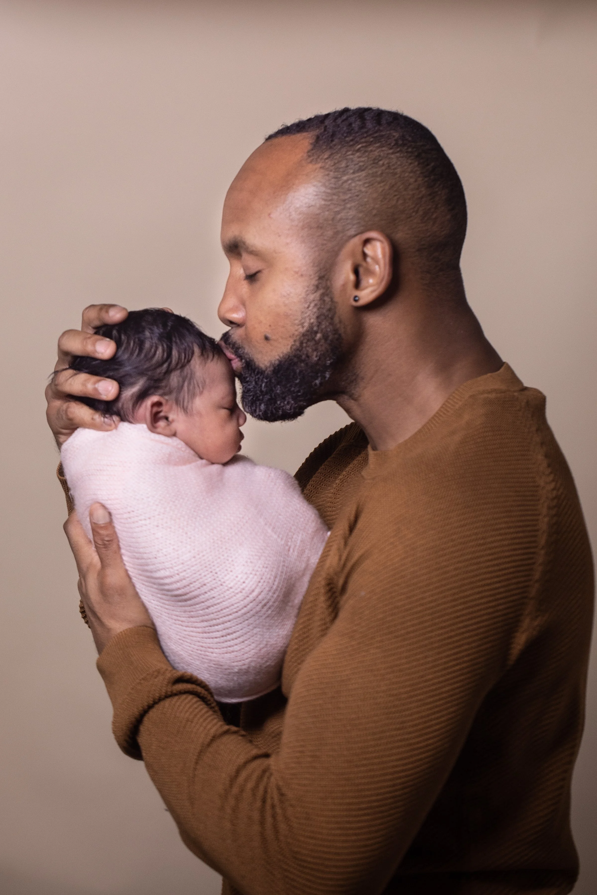 Father tenderly kissing his newborn baby daughter during an at-home newborn photography session with dad in Bromley, London by Kate See.