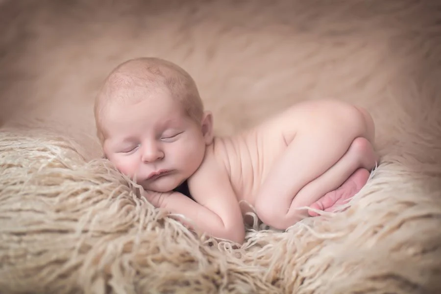 A sleeping newborn baby with closed eyes, resting on a fluffy beige blanket.