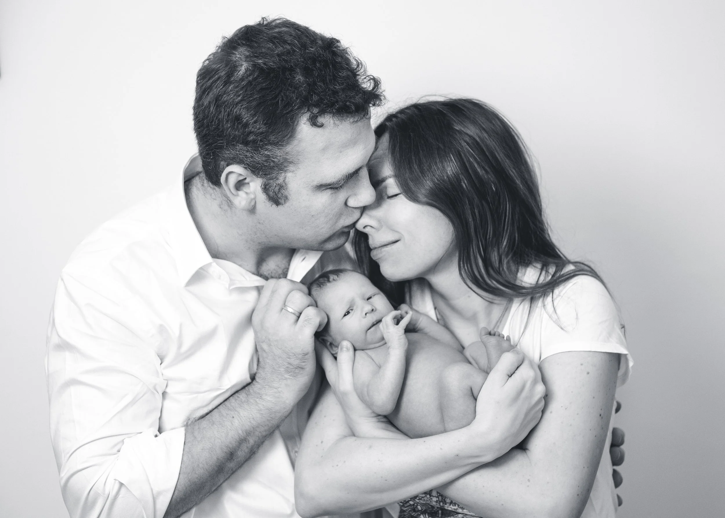 A black and white photo of a happy family, a man and woman holding their two babies close, with the man and woman leaning their foreheads together in a loving gesture.