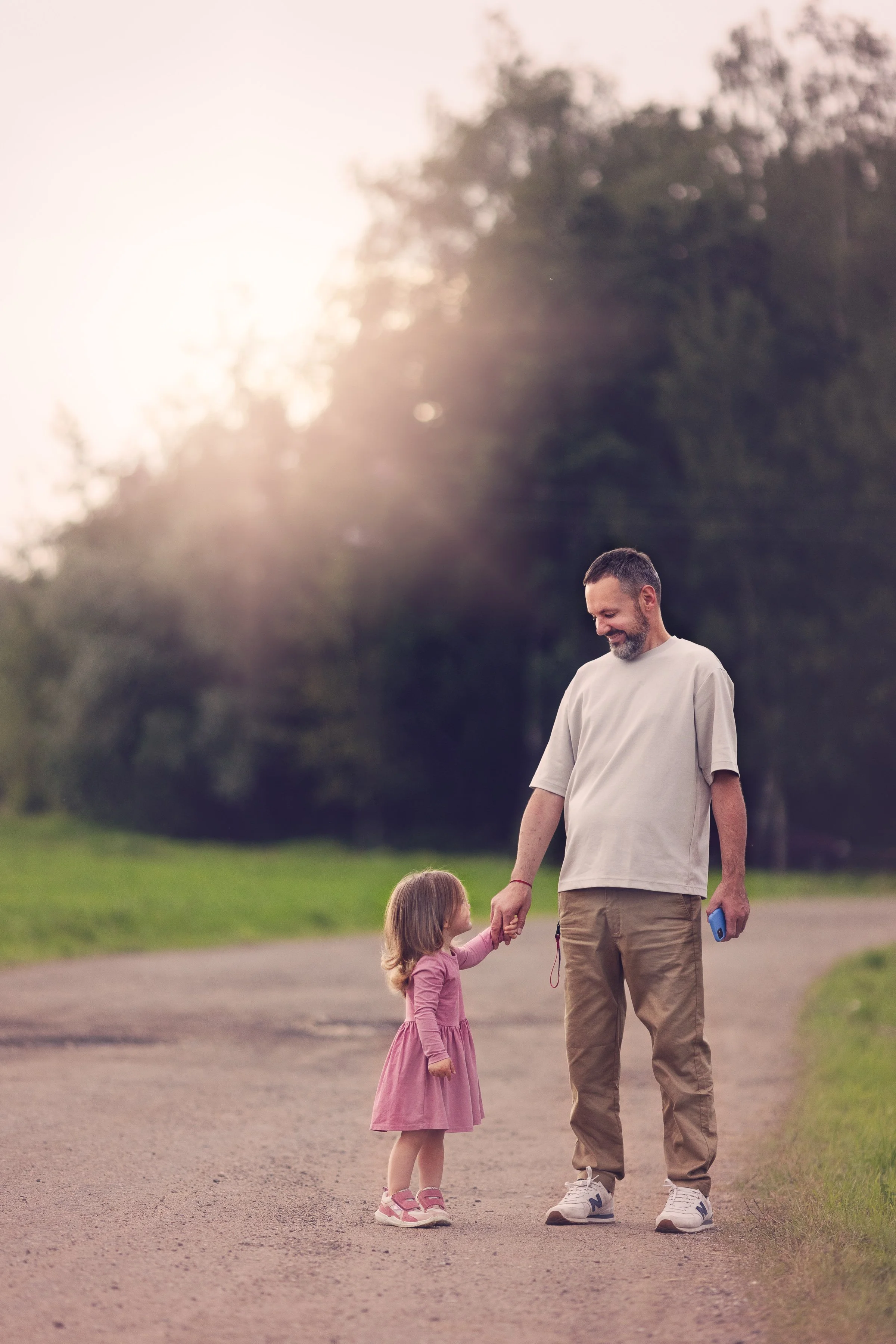 A man walking with a young girl in a park during sunset, holding hands and smiling.