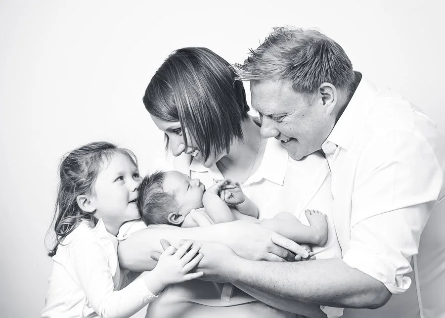 Black and white photo of a family, a man and woman with three young children, appearing to share a happy moment together.