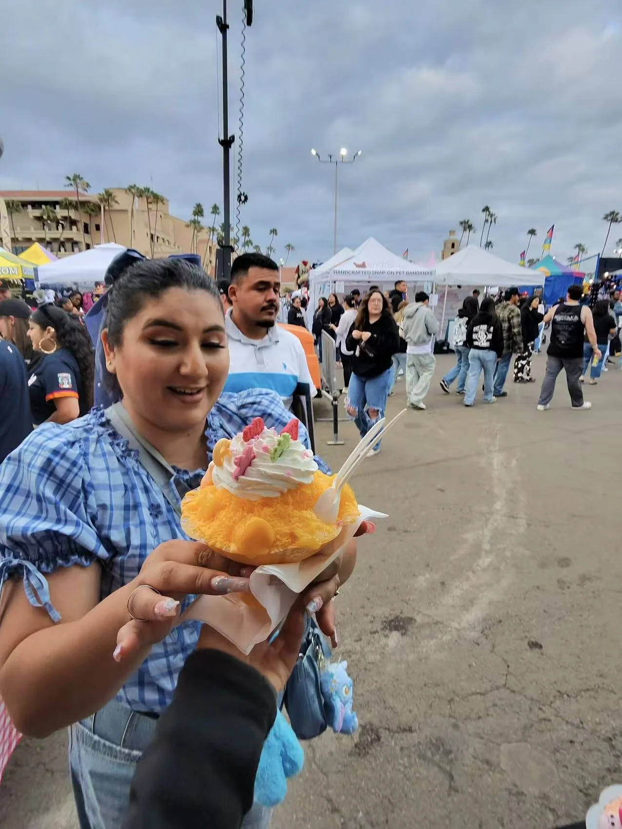 Woman holding shaved ice dessert with whipped cream and colorful toppings at outdoor festival
